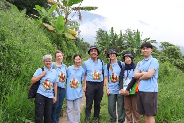 Kelompok 7 orang berbaju biru dengan gambar ayam berpose di jalur hijau di pegunungan.
